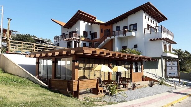 A two-story building with a cafe area featuring outdoor seating and umbrellas. - Vila Tamu (Imbituba)