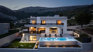 Una casa moderna de dos pisos con piscina, mobiliario exterior y vistas del paisaje circundante.