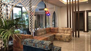 A modern living area with a sectional sofa, a patterned ottoman, and a large mirror. - PREMIUM SUNRISE (Golem)