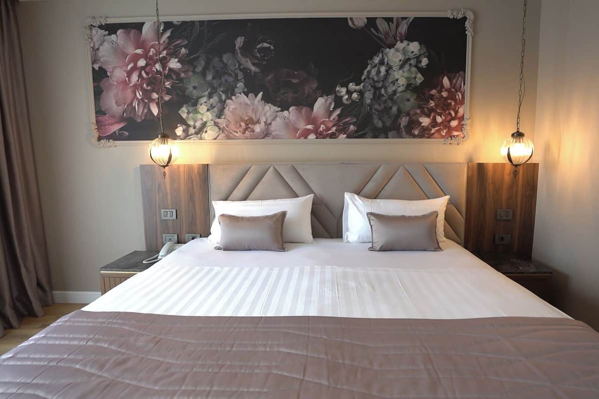 A hotel room with a large bed, two bedside tables, a floral artwork above the bed, and two wall-mounted lamps.