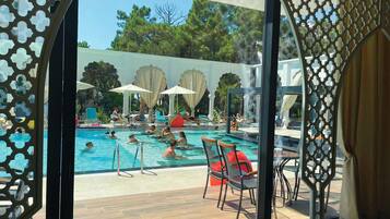 Zona de piscina con sillas de descanso y sombrillas, rodeada por una valla decorativa.