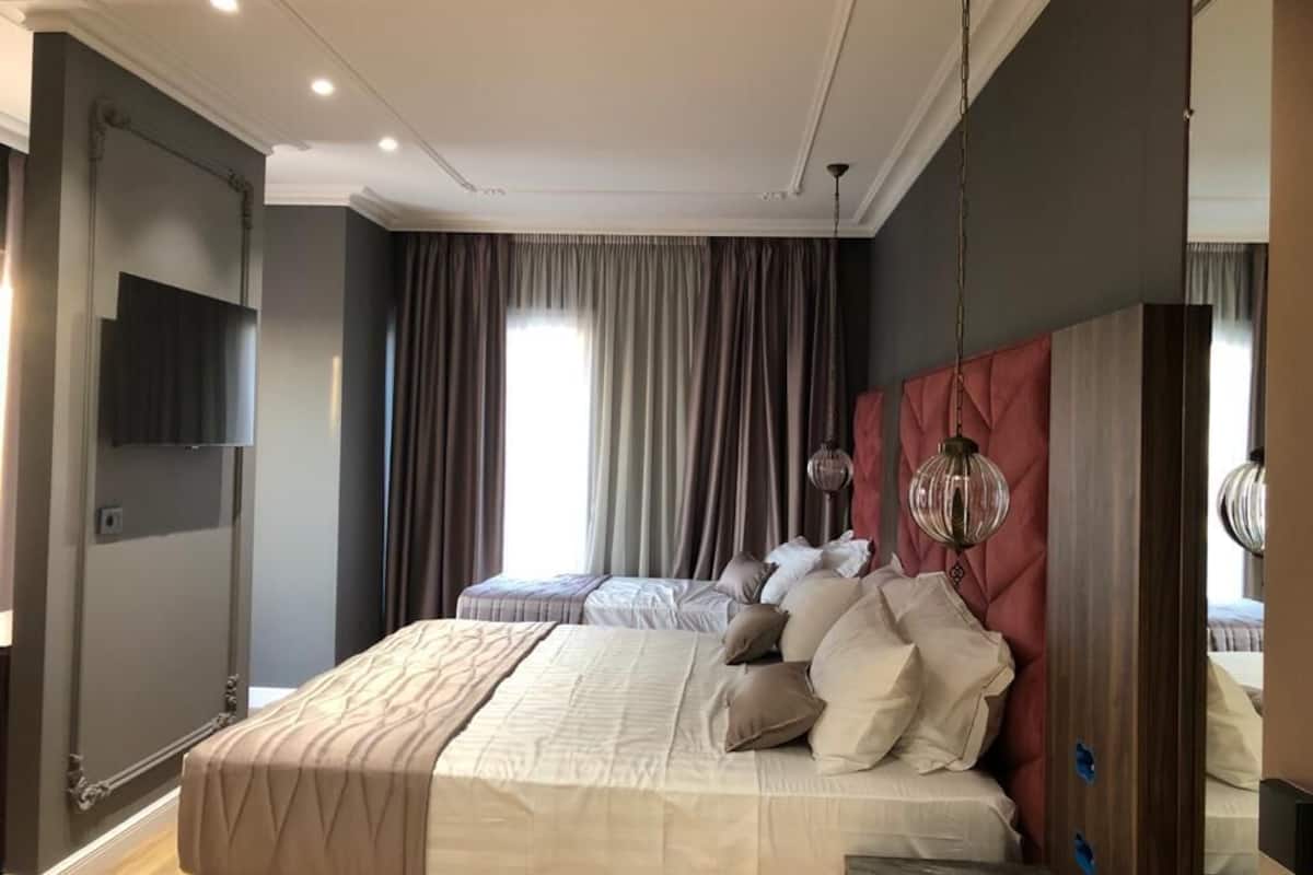 A modern hotel room with a large bed, a TV mounted on the wall, and a large window with curtains.