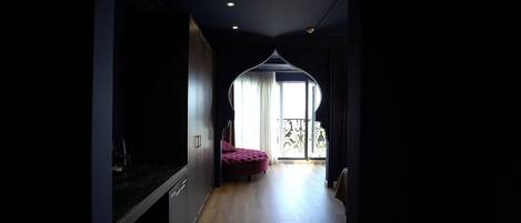 A hallway leading to a balcony with a red ottoman and a sliding glass door.