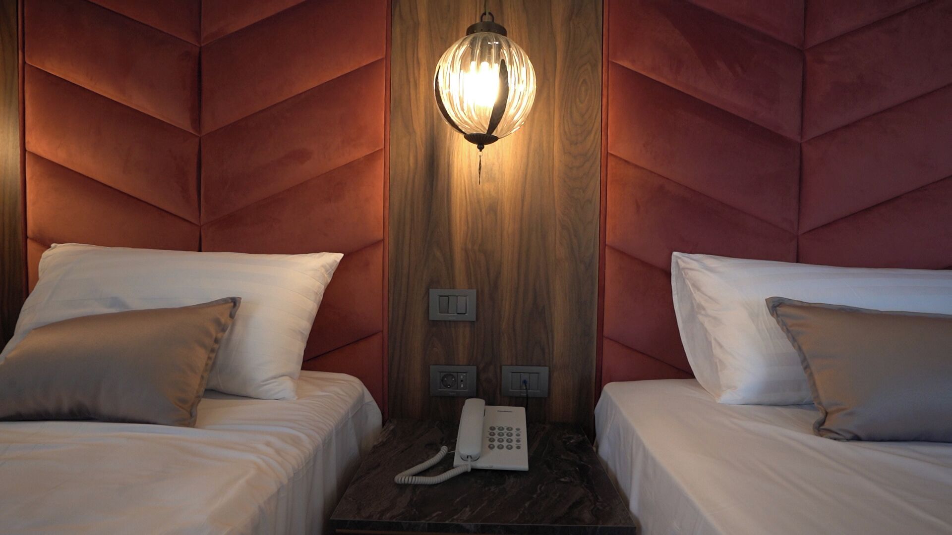 Een hotelkamer met twee bedden, een houten accentmuur, een wandtelefoon en een hanglamp.