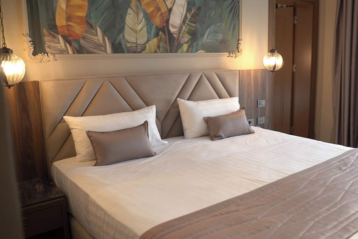 A neatly made bed with a headboard, two bedside lamps, and a painting above the bed.