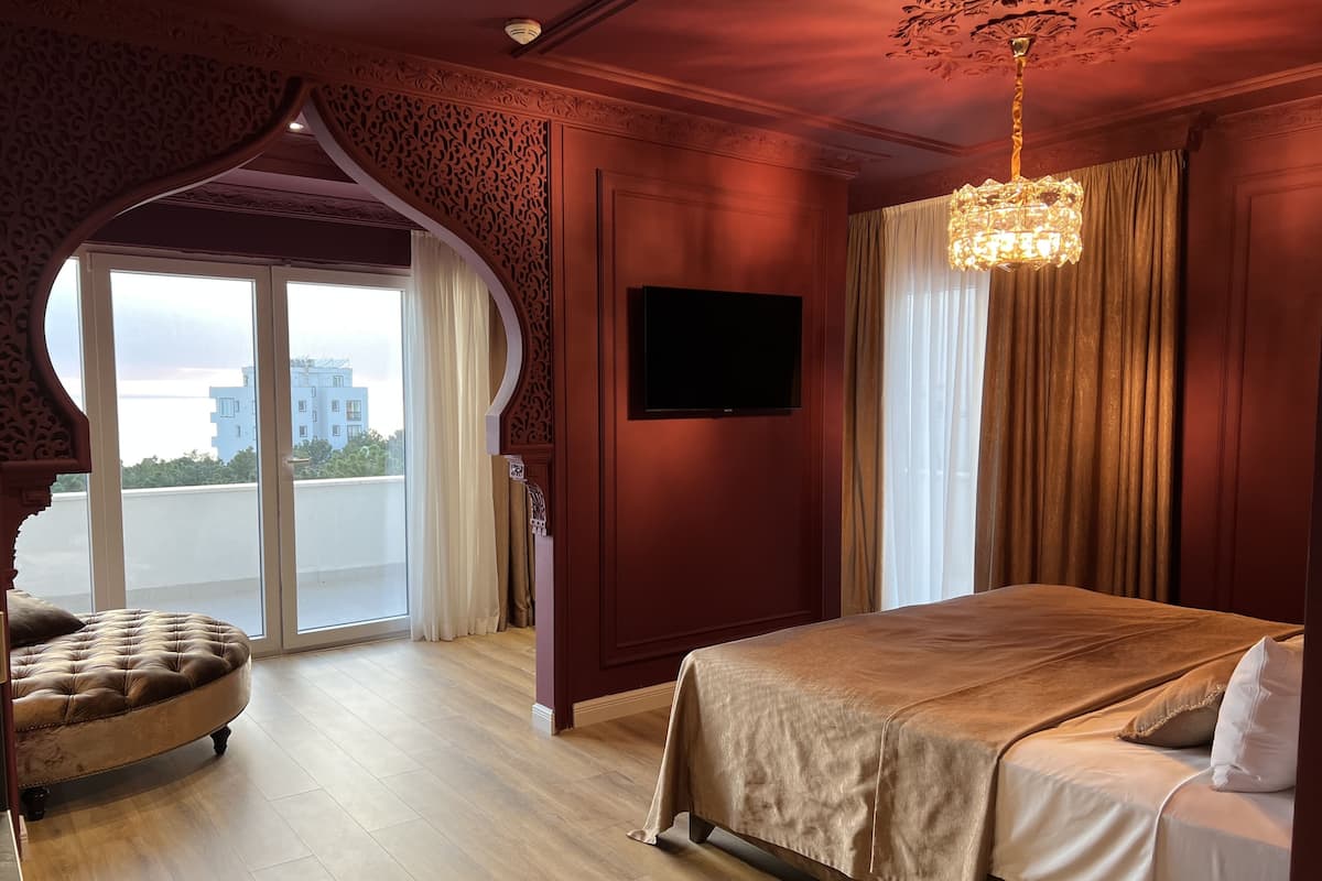 A bedroom with a large bed, a TV mounted on the wall, and a balcony with curtains.