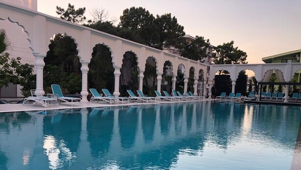 A pool with lounge chairs and a white building with arches. - PREMIUM SUNRISE (Golem)