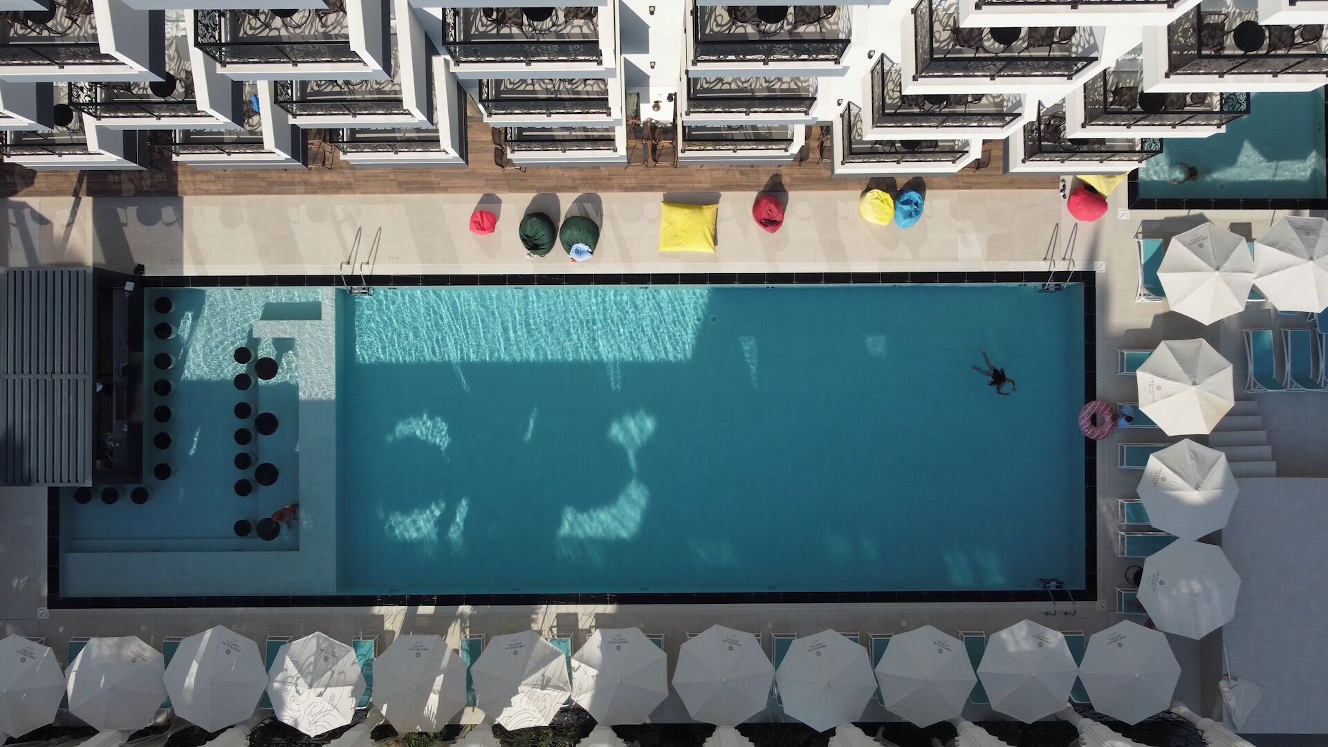 An aerial view of a swimming pool with lounge chairs and umbrellas around it.