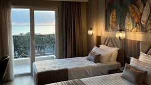 A hotel room with two beds, a view of the sea through a balcony, and a painting on the wall. - PREMIUM SUNRISE (Golem)