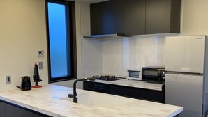 A modern kitchen with a central island, built-in appliances, and a large window. - SkyBlueVilla (読谷村)