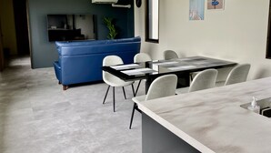 A modern dining area with a long table, white chairs, and a grey countertop with a soap dispenser. - SkyBlueVilla (読谷村)