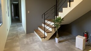 A modern staircase with a minimalist design, a potted plant, and a fire extinguisher near the bottom. - SkyBlueVilla (読谷村)