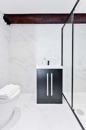 A modern bathroom with a marble floor, a dark wooden beam ceiling, a glass shower enclosure, and a white toilet. - Beautiful 1 Bedroom Apartment in Burton-on-Trent (Burton upon Trent)