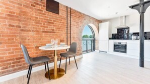 A modern kitchen with a brick wall, a round dining table with two chairs, and a view through an archway.