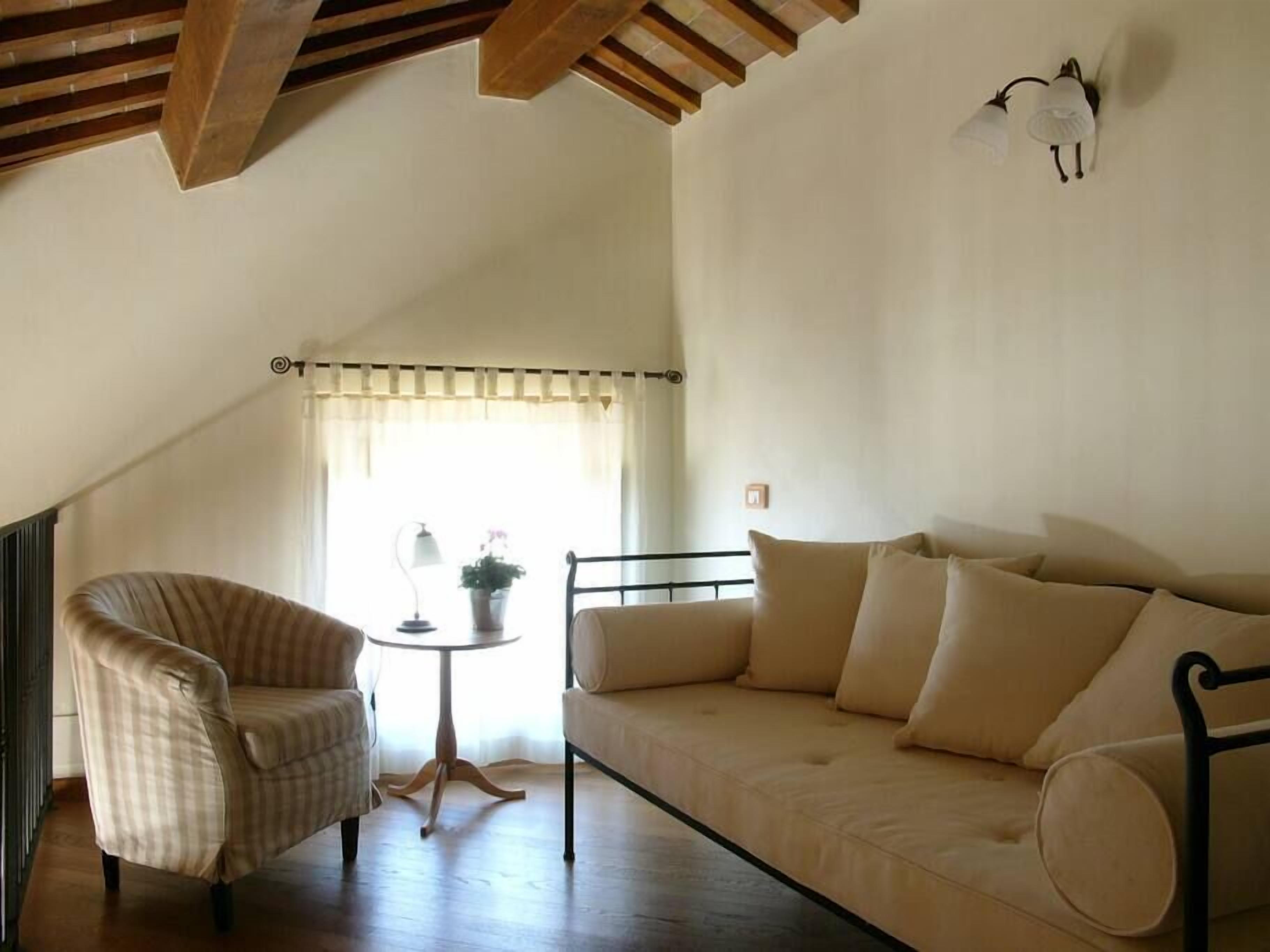 Una sala de estar acogedora con un sillón a rayas, un sofá color beige y una pequeña mesa redonda con una lámpara y una planta en maceta.