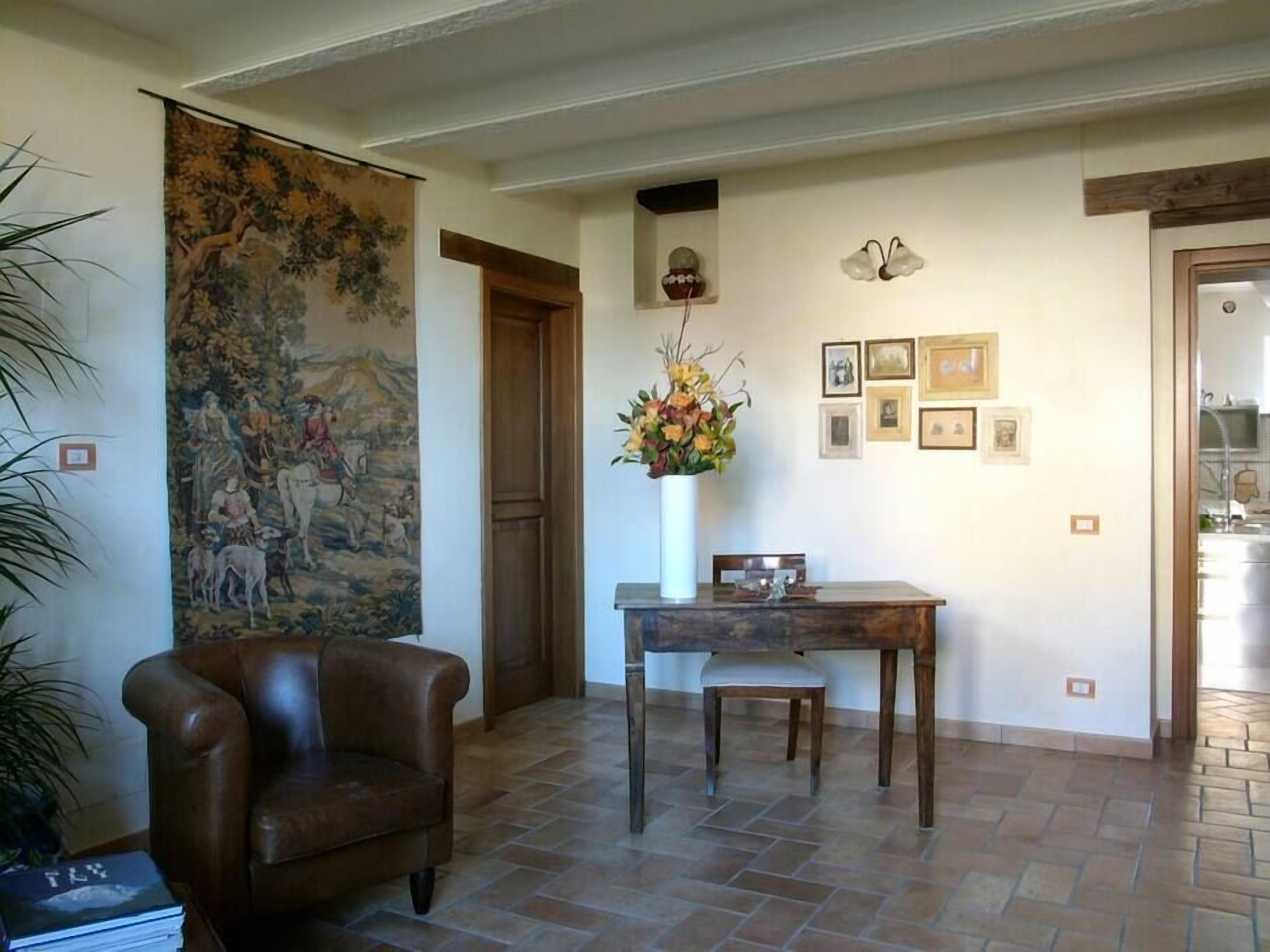 Una sala de estar con un sofá de cuero marrón, una mesa de comedor con un florero y un tapiz grande en la pared.