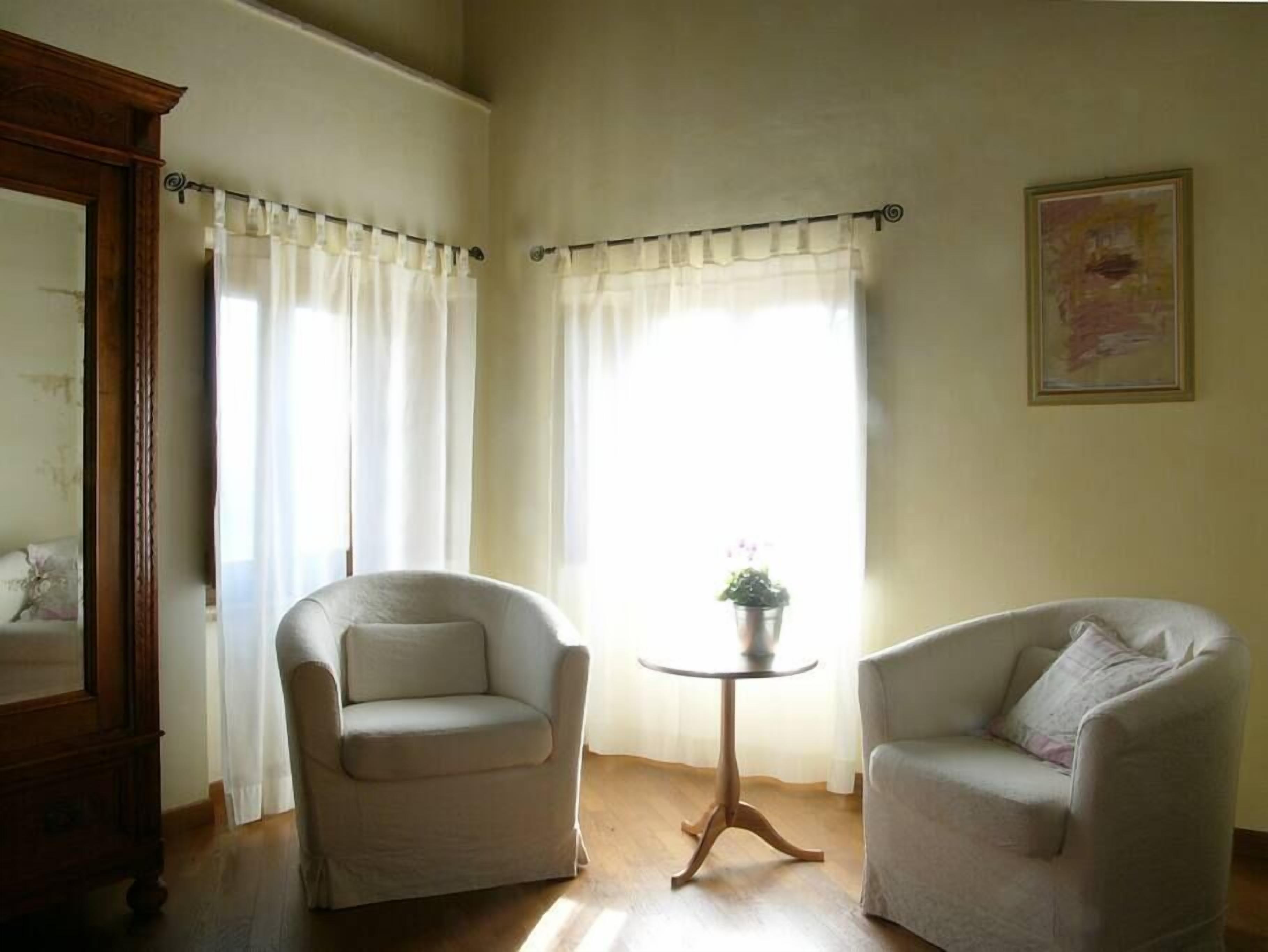Une pièce avec deux fauteuils, une petite table ronde et une fenêtre avec des rideaux.