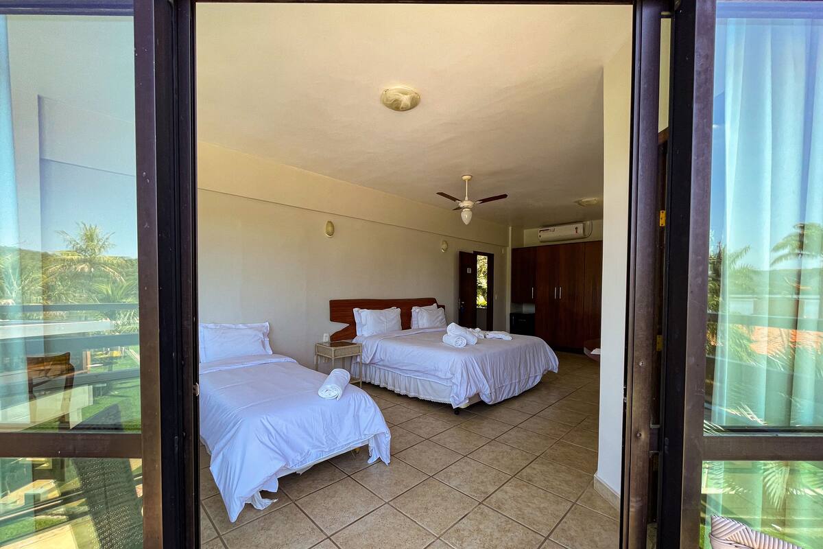 Ein Hotelzimmer mit zwei Betten, einem Deckenventilator und Blick ins Freie durch eine Glastür.