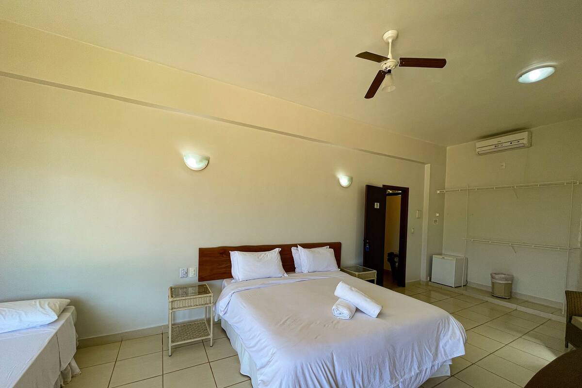 Ein Hotelzimmer mit einem großen Bett, zwei Nachttischen, einem Deckenventilator und einer Tür zu einem anderen Raum.