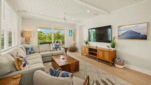 A modern living room with a sectional sofa, a wooden coffee table, a TV, and a large window with a view of greenery. - Eco Smart Home, Canalfront with Pool! (Cortez)