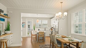 A modern kitchen with white cabinets, a wooden dining table, and a hanging light fixture. - Eco Smart Home, Canalfront with Pool! (Cortez)