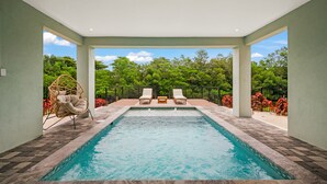 A swimming pool with two lounge chairs and a wicker chair, surrounded by a paved deck and a view of lush greenery. - Eco Smart Home, Canalfront with Pool! (Cortez)