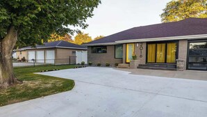 Una casa moderna de dos pisos con garaje, entrada para vehículos y un árbol en primer plano.