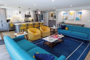 A modern living room with a blue sofa, yellow chairs, and a kitchen in the background.