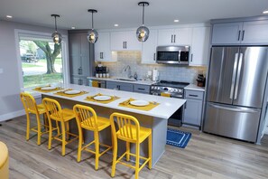 A modern kitchen with a central island, stainless steel appliances, and yellow chairs.