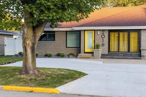 Un bĂątiment moderne Ă deux Ă©tages, dotĂ© dâune porte jaune, de grandes fenĂȘtres et dâun arbre dans le jardin.