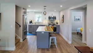 A modern kitchen with a central island, stainless steel appliances, and a view into the adjacent bedroom.