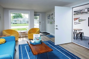 Ein modernes Wohnzimmer mit einem blauen Sofa, gelben Sesseln, einem Couchtisch und einem Willkommensschild.