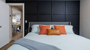 Un dormitorio con cama, cabecera y vista a la cocina.