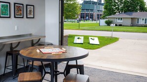 Una habitación con una mesa redonda, sillas, un ventanal con vista a un edificio y un jardín.