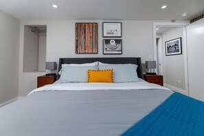 Een moderne slaapkamer met een groot bed, twee nachtkastjes, een hoofdbord en kunstwerken aan de muur.