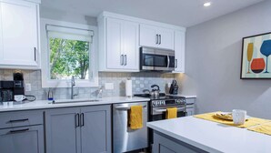 Una cocina moderna con armarios blancos, electrodomésticos de acero inoxidable y una ventana con vistas a árboles.