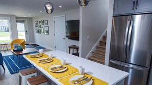 Una cocina moderna con un refrigerador de acero inoxidable, un comedor con manteles individuales amarillos y una escalera que conduce a otro nivel.