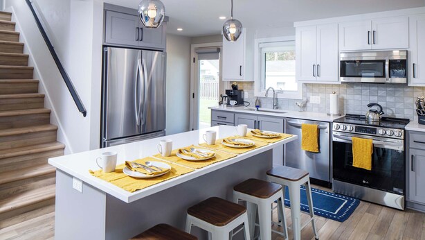 Una cocina moderna con una isla central, electrodomésticos de acero inoxidable y una escalera de madera.
