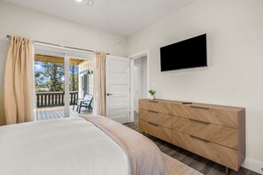Quarto com cama, penteadeira, televisão e varanda com cadeira.