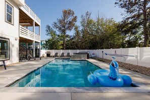 Uma piscina com uma bóia azul inflável, uma área de estar coberta ao ar livre e um edifício branco com varanda.