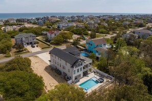 Uma grande casa de dois andares com piscina, situada numa zona residencial com casas e árvores.