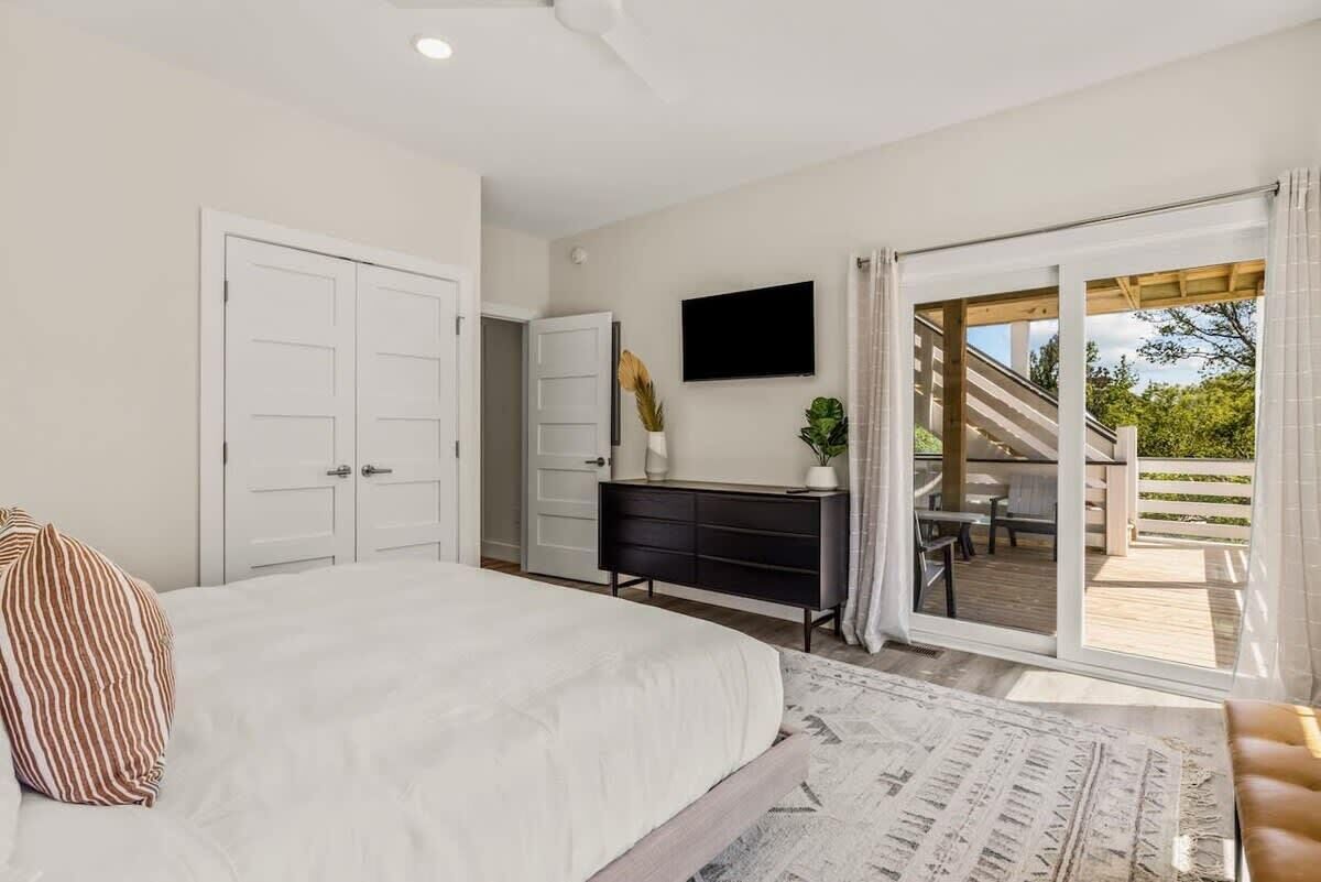 A bedroom with a large bed, a dresser, a TV, and a sliding glass door leading to an outdoor patio.