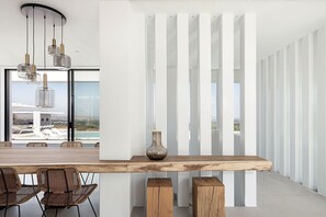 Zona pranzo moderna con tavolo in legno, sedie in vimini e vista su piscina e edifici.