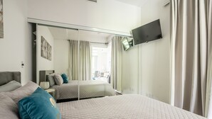 Habitación de hotel con una cama grande, un televisor montado en la pared y un balcón al que se accede mediante una puerta corrediza.