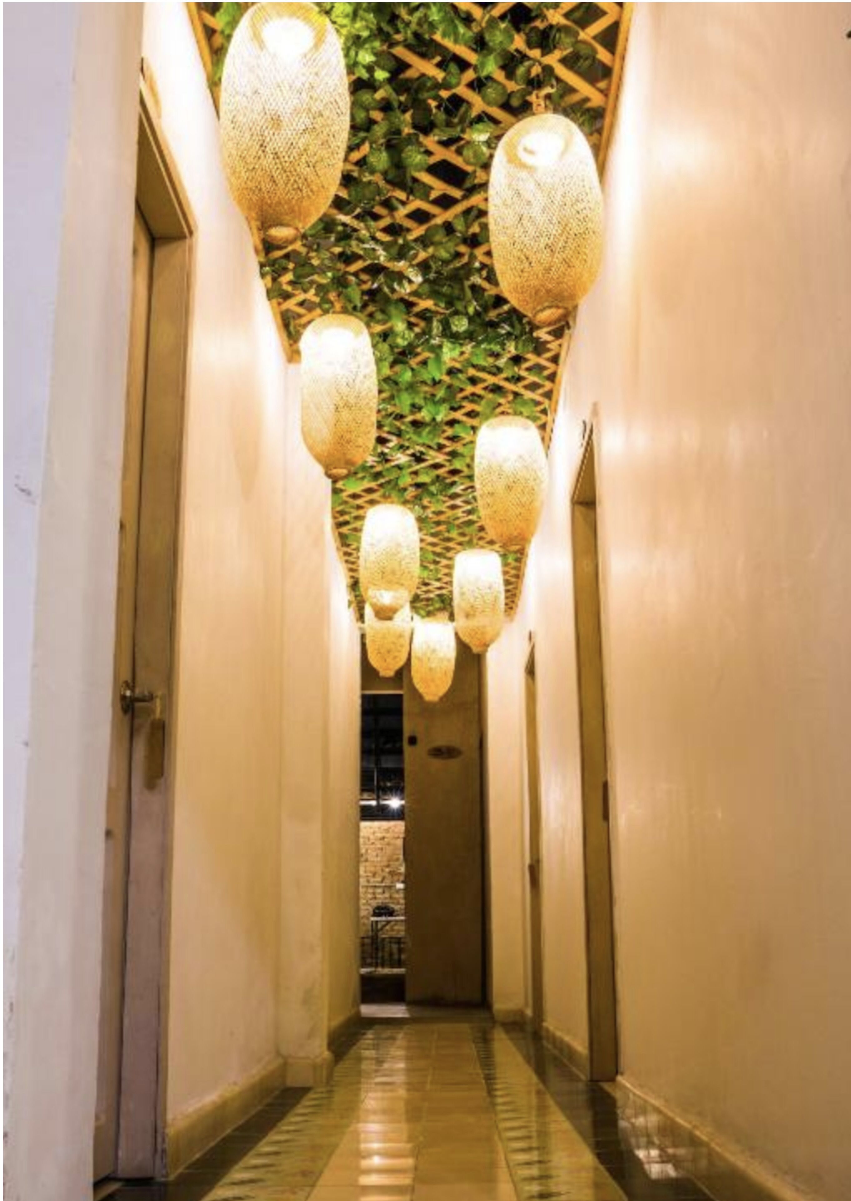 A hallway with multiple hanging lanterns and a green leafy ceiling.
