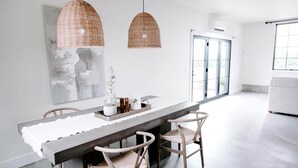 A modern dining area with a long table, wicker pendant lights, and a large abstract painting. - Sycamore Hill Guesthouse (Oklahoma County)
