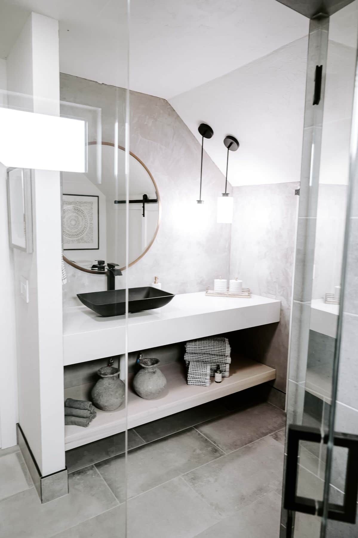 Une salle de bain moderne avec un grand miroir, un lavabo noir et deux lampes suspendues.