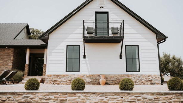 A white building with a stone base, a balcony, and a door. - Sycamore Hill Guesthouse (Oklahoma County)