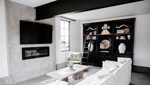 A modern living room with a large flat-screen TV, a sofa, a coffee table, and a black entertainment unit with various decorative items. - Sycamore Hill Guesthouse (Oklahoma County)