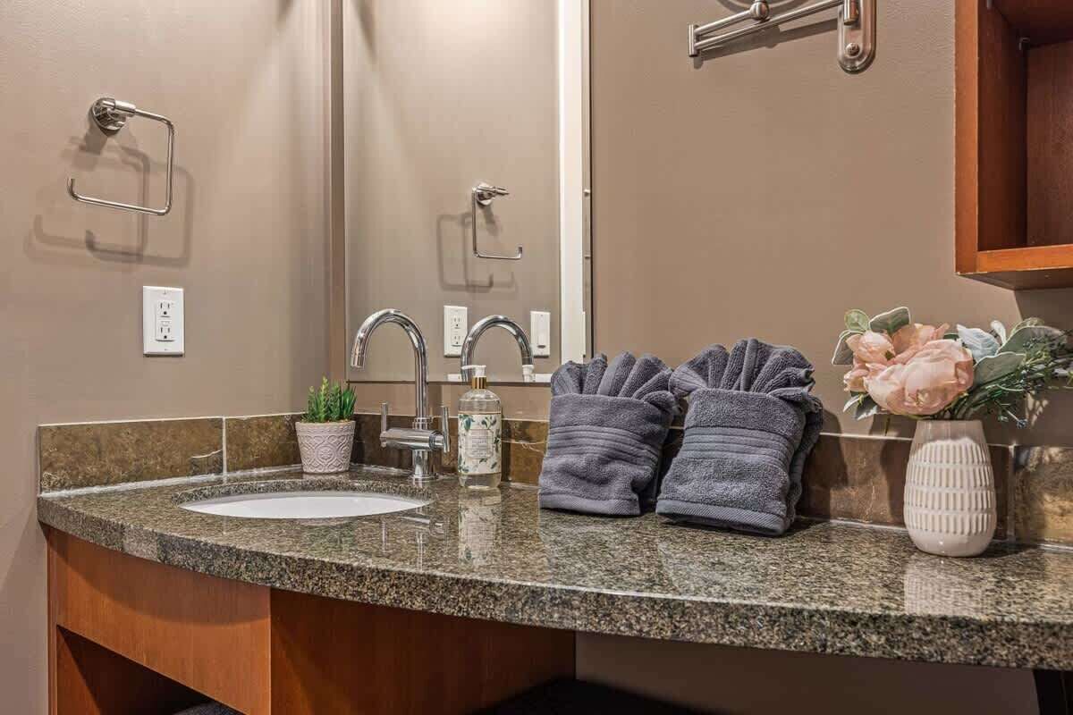 A bathroom with a granite countertop, a sink, a mirror, a towel rack, a potted plant, and a vase with flowers.
